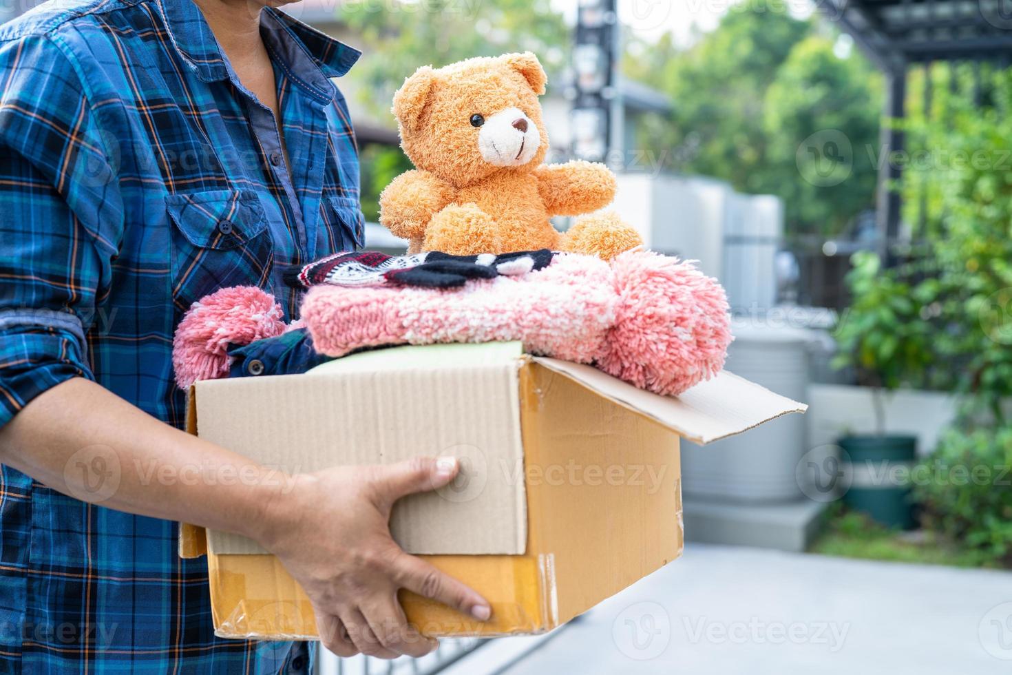 Kleiderspendenbox mit gebrauchter Kleidung und Puppe zu Hause halten, um die Hilfe für arme Menschen in der Welt zu unterstützen. foto