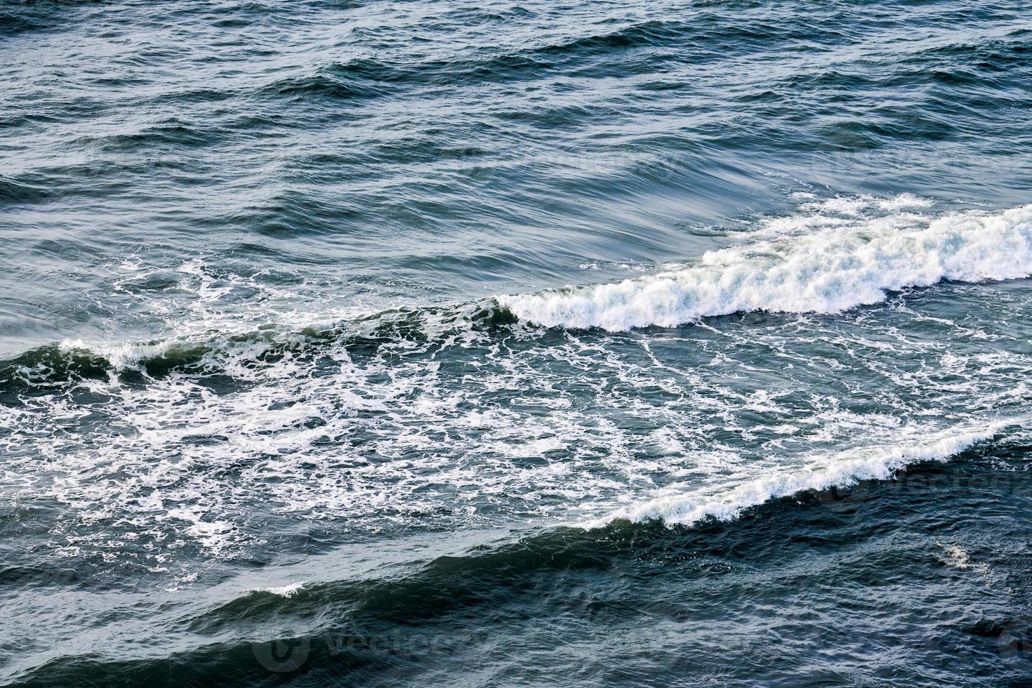 tiefblaues meerwasser, das mit schaumigen wellen spritzt, dunkelblaue gewellte ozeanwasseroberfläche, stürmisches meer foto