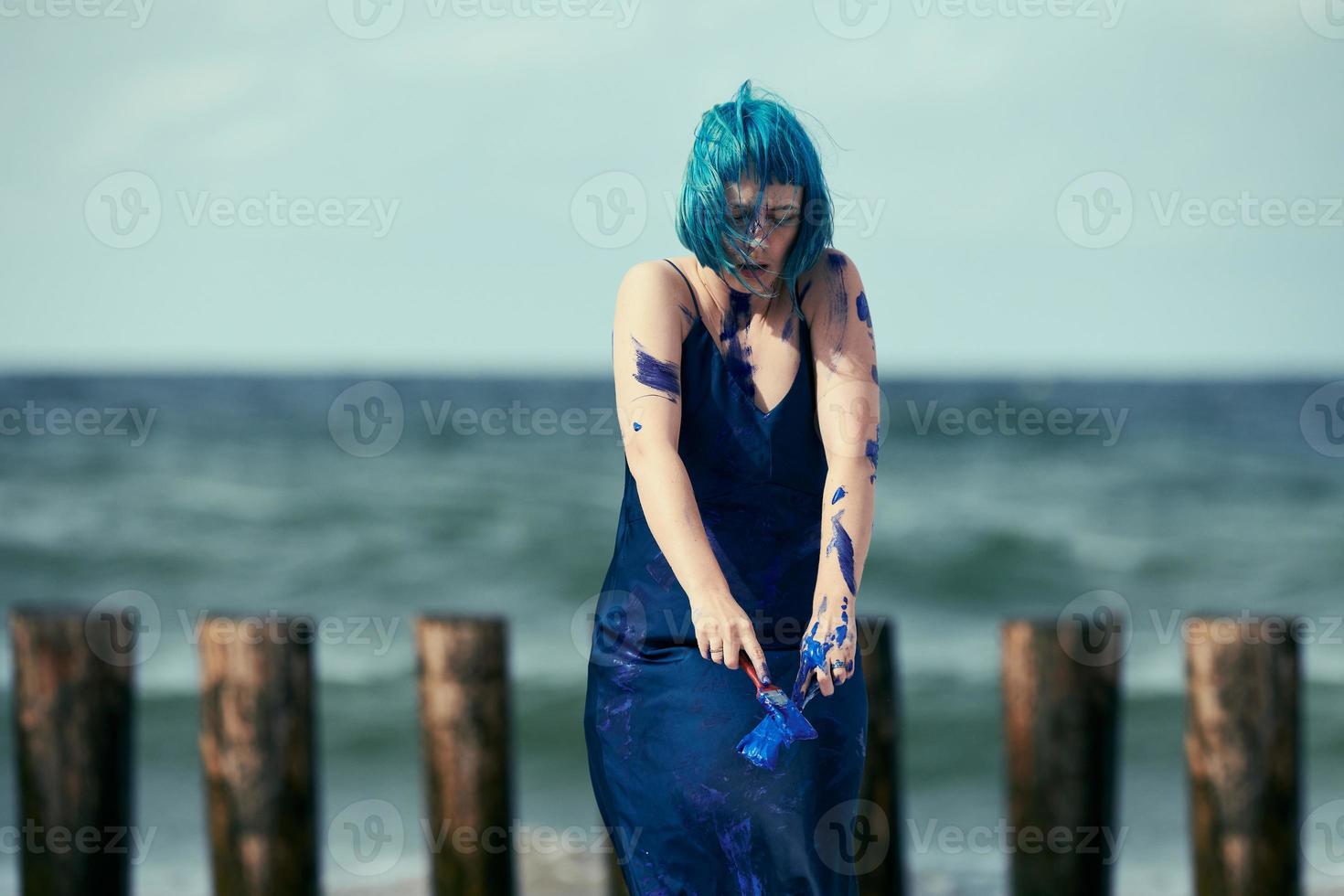 Künstlerische blauhaarige Performance-Künstlerin im Kleid, das mit blauen Gouachefarben auf ihrem Körper verschmiert ist foto