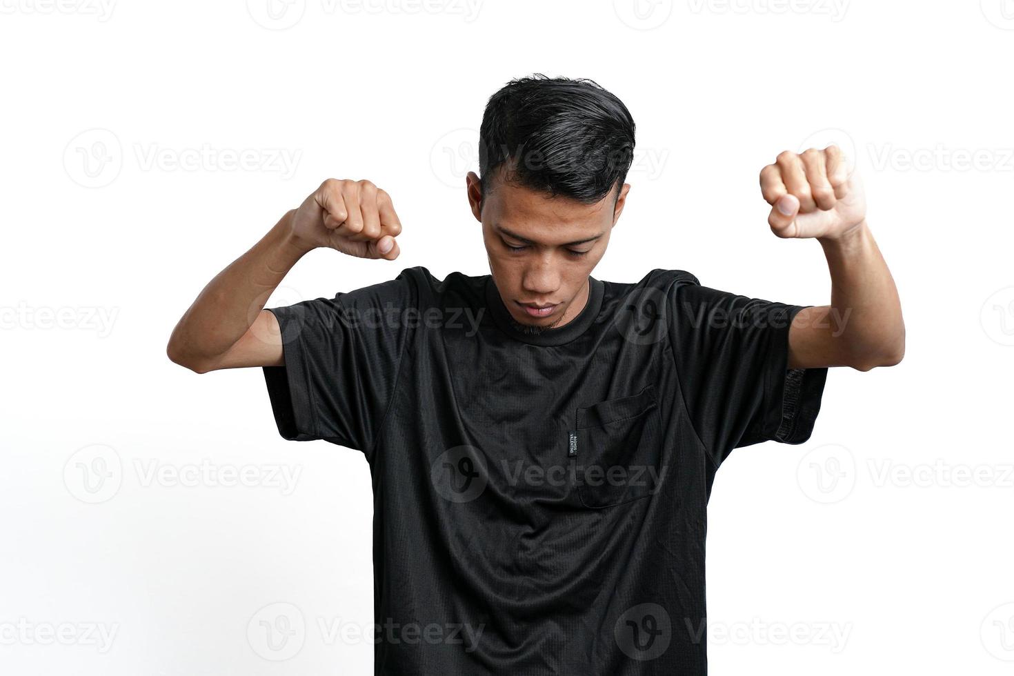 asiatischer Mann mit schwarzem Trainings-T-Shirt, der eine starke Haltung mit erhobenen Armen und Muskeln zeigt. durch weißen Hintergrund isoliert foto