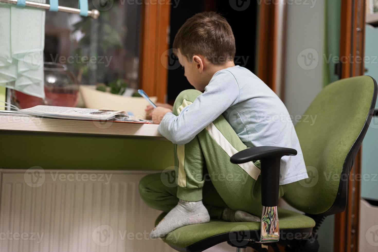 kind junge lernt zu hause und macht schulhausaufgaben, fernunterricht, sitzt am tisch. foto