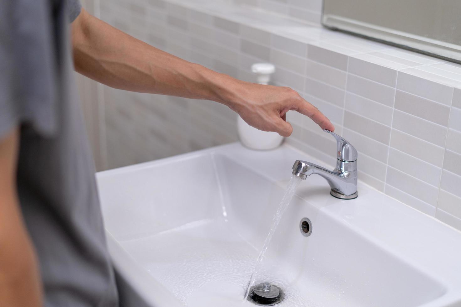 der Wasserhahn im Badezimmer mit fließendem Wasser. Mann dreht immer wieder das Wasser ab, um Wasserenergie zu sparen und die Umwelt zu schonen. wasser sparen konzept foto