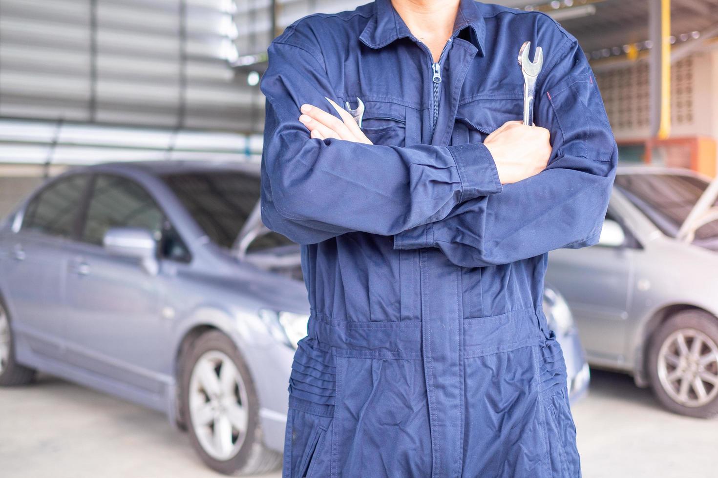 Autoservicetechniker in Uniform, der mit einem Schraubendreher auf dem Hintergrund eines Autos steht und das Auto repariert und wartet. Werkstatt- und Autoteile-Ersatzkonzept foto