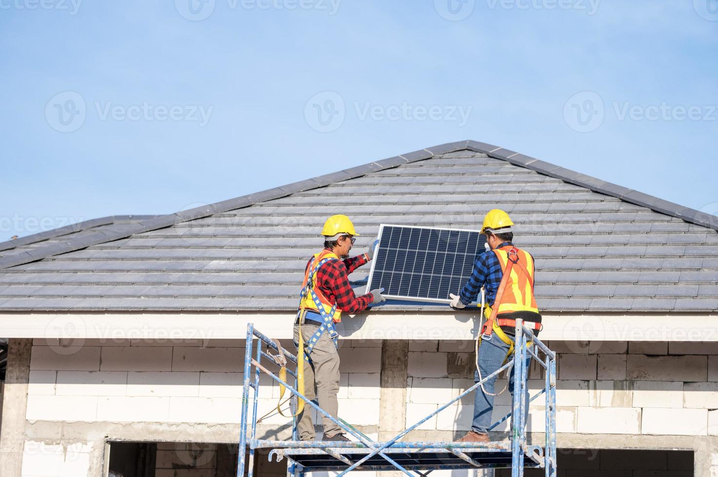 ein team asiatischer techniker installiert sonnenkollektoren auf dem dach eines hauses. Querschnittsansicht des Baumeisters im Helm, der ein Solarpanel-Systemkonzept für erneuerbare Energien installiert foto