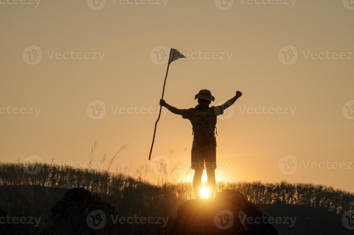 Silhouette der amerikanischen Pfadfinder mit Flagge auf dem Berg mit blauem Himmel und Sonnenlicht. Es symbolisiert die Führung der Pfadfinder beim Trekking, die ihre Ziele und Ziele erreicht. foto