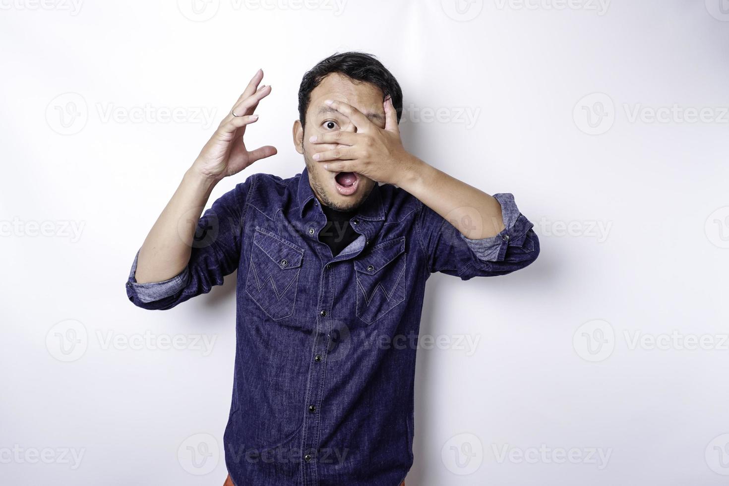 lustiger offensichtlicher spähender asiatischer mann im blauen hemd lokalisiert auf weißem hintergrund. foto