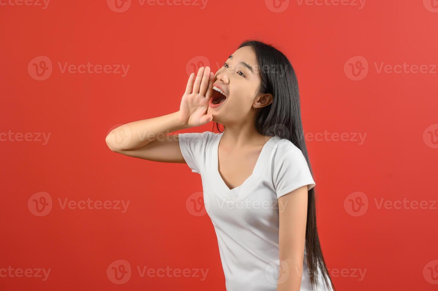 porträt einer jungen asiatischen frau in weißem t-shirt, die geschichte schreit oder eine ankündigung isoliert auf rotem hintergrund macht foto