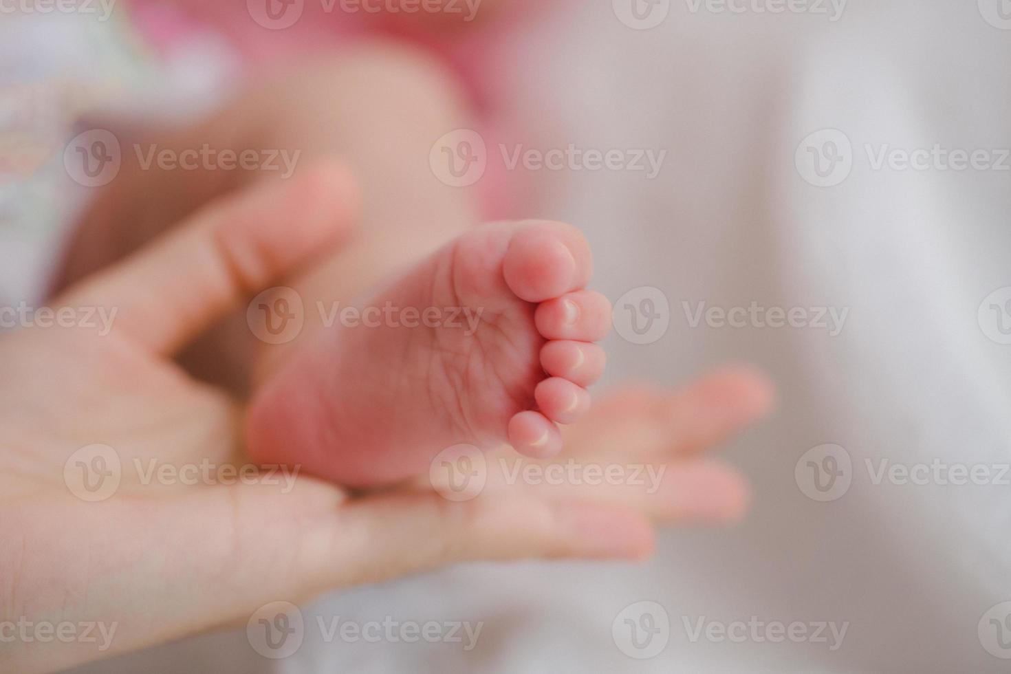 nahaufnahme mutter, die fuß neugeborenes mädchen in einem raum hält. entzückendes kind ruht auf weißen bettlaken und starrt friedlich in die kamera. Säuglings-, Gesundheitswesen und Pädiatrie, Säuglingskonzept. foto