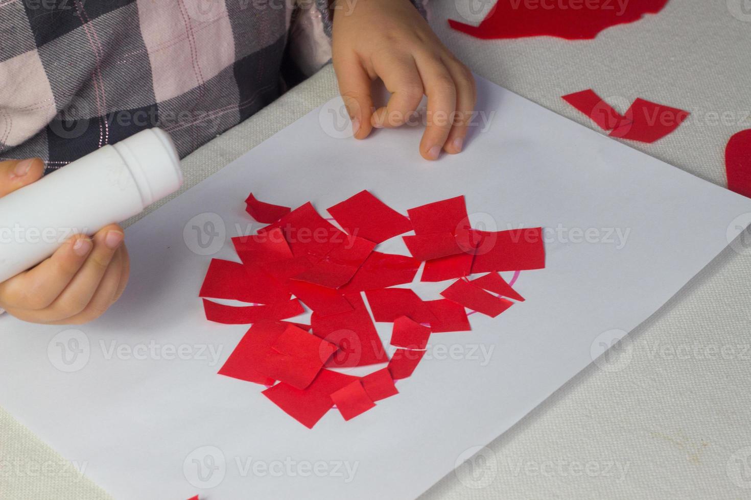 Kleines Mädchen, das rote Herzapplikationen mit Papier und Kleber auf weißem Blatt macht, Valentinstagsgrußkarte, Weihnachtsgeschenk für Muttertag, handgemachtes Kindergeschenk, Liebessymbol mit Papier, Kleinkindaktivität foto