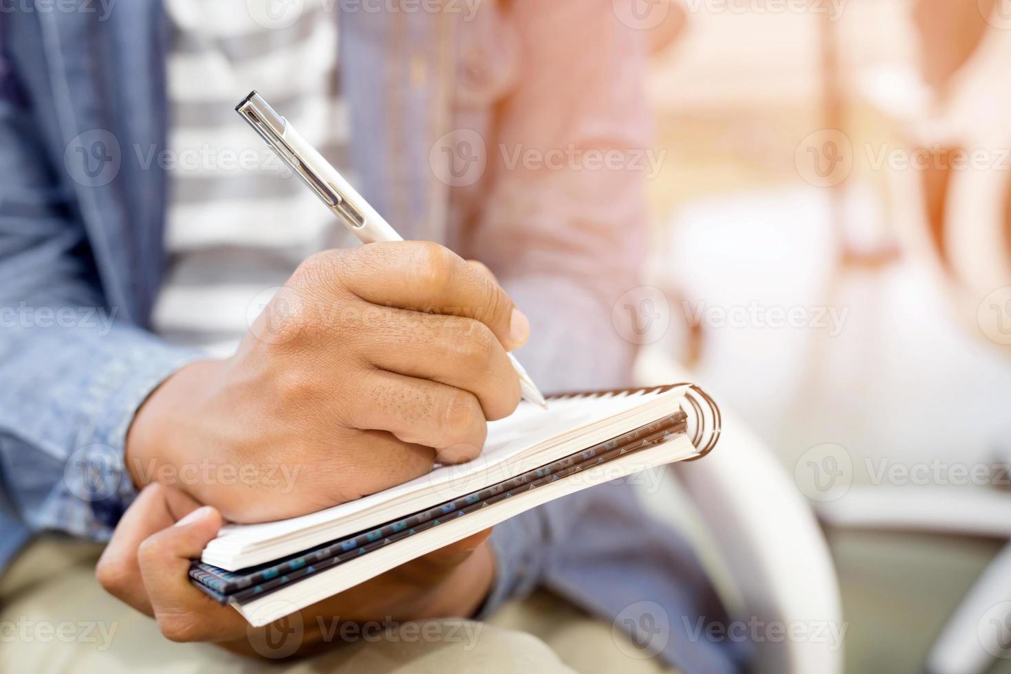 nahaufnahme hand menschen mann sitzen auf einer treppe. Verwenden Sie einen Stift, der einen Vorlesungsnotizblock in das Buch in der Parköffentlichkeit schreibt. foto