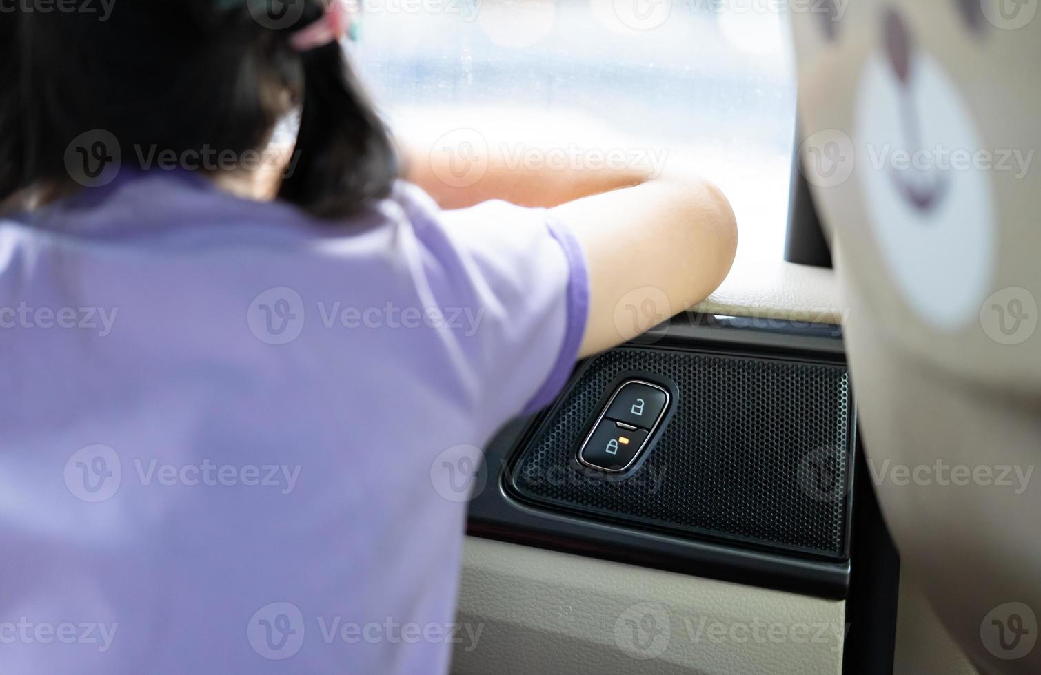 Kleines asiatisches 5-jähriges Mädchen schaut nach draußen durch den Autofensterspiegel mit dem Symbol für das Autotürschloss neben ihr. foto