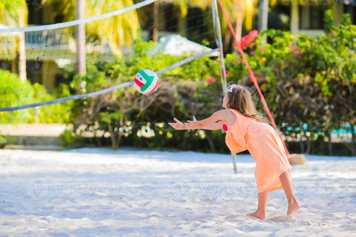 Kleines aktives Mädchen, das Volleyball am Strand mit Ball spielt. sportliches Flid, das Strandspiel im Freien genießt foto