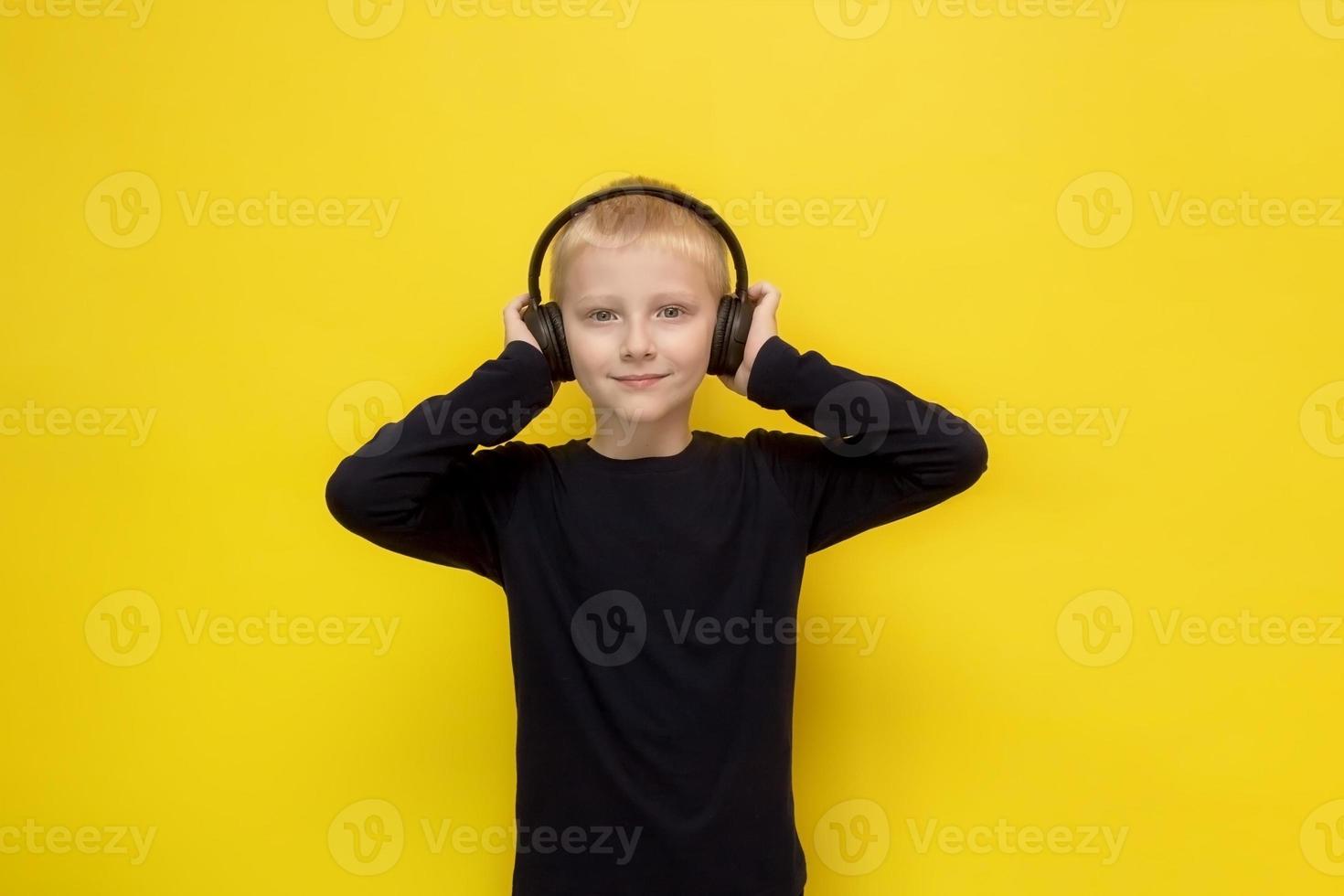 süßer blonder junge, der musik oder podcast über kopfhörer auf gelbem hintergrund hört foto