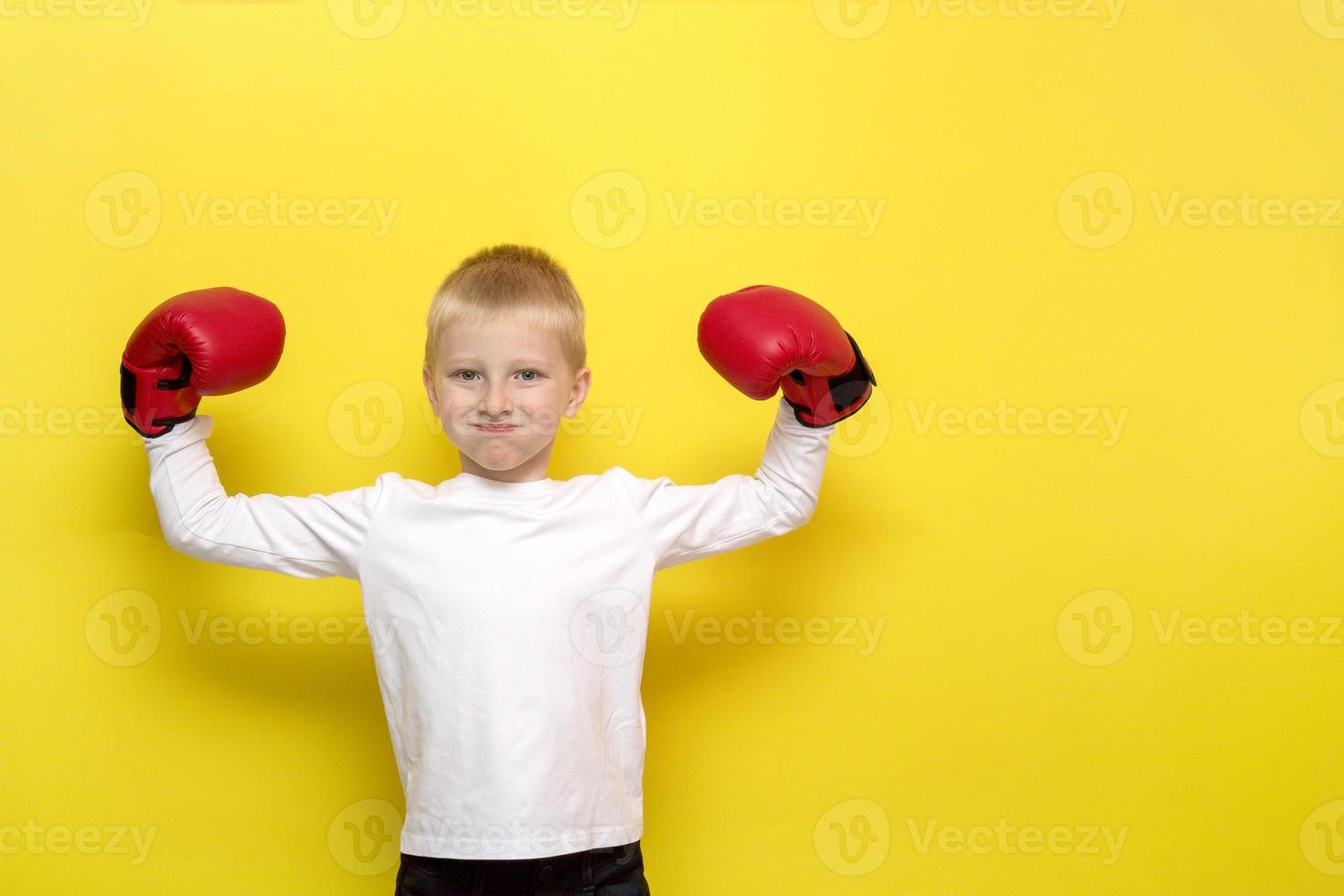 Der blonde Junge in roten Boxhandschuhen zeigt einen Boxer, der seine Hände hebt und seine Wangen auf gelbem Hintergrund aufbläst foto