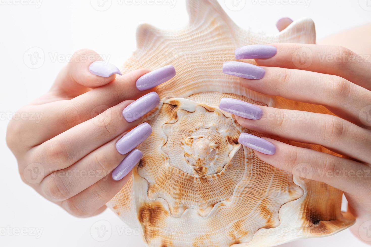 Hand mit langen violetten gepflegten Nägeln und Muscheln foto