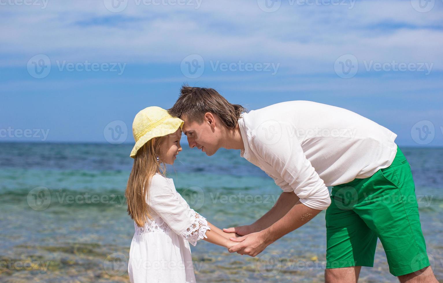 glücklicher vater und seine entzückende kleine tochter am strand an einem sonnigen tag foto