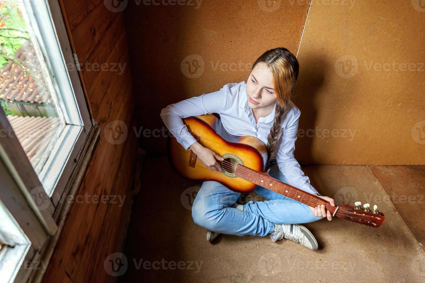 Junge Hipster-Frau, die auf dem Boden sitzt und zu Hause Gitarre spielt. Teenager-Mädchen lernen, Lieder zu spielen und Musik in ihrem Zimmer zu schreiben. hobby, lebensstil, entspannen, instrument, freizeit, bildungskonzept. foto