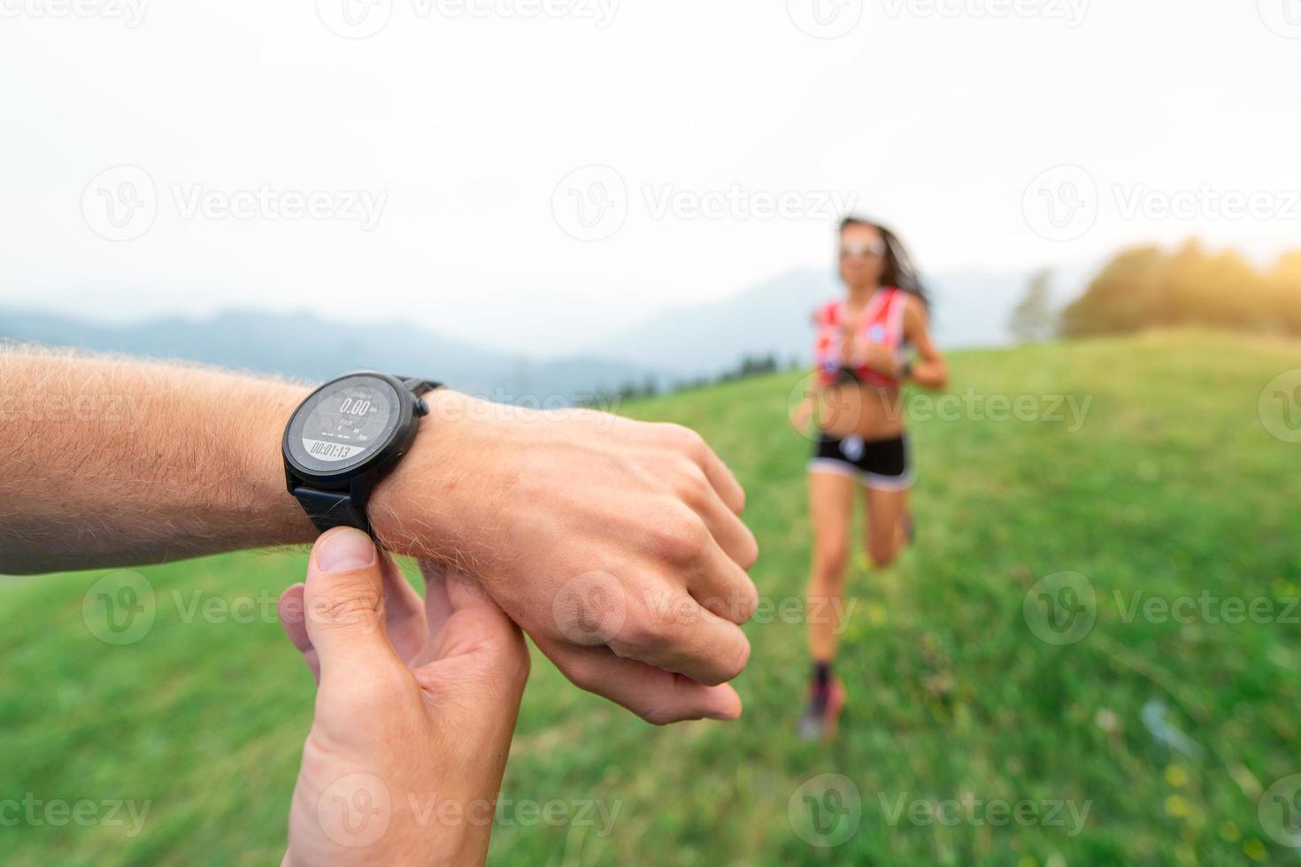 Sporttrainer hält die Stoppuhr, während er ein Mädchen trainiert, das in der Natur läuft foto