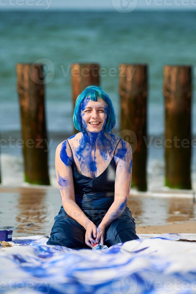 Künstlerische blauhaarige Performance-Künstlerin im Kleid, das mit blauen Gouachefarben auf ihrem Körper verschmiert ist foto