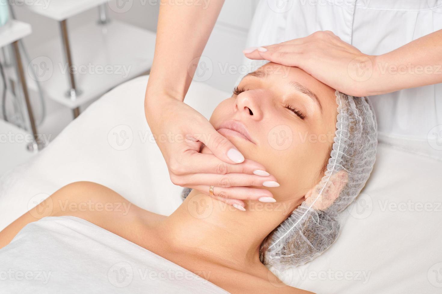 Kosmetikerin massiert Crememaske in die Gesichtshaut der Frau zur Verjüngung, Verfahren im Schönheitssalon foto