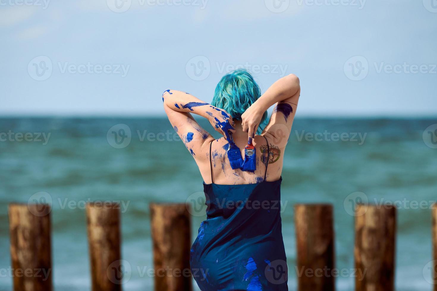 Künstlerische blauhaarige Performance-Künstlerin im Kleid, das mit blauen Gouachefarben auf ihrem Körper verschmiert ist foto