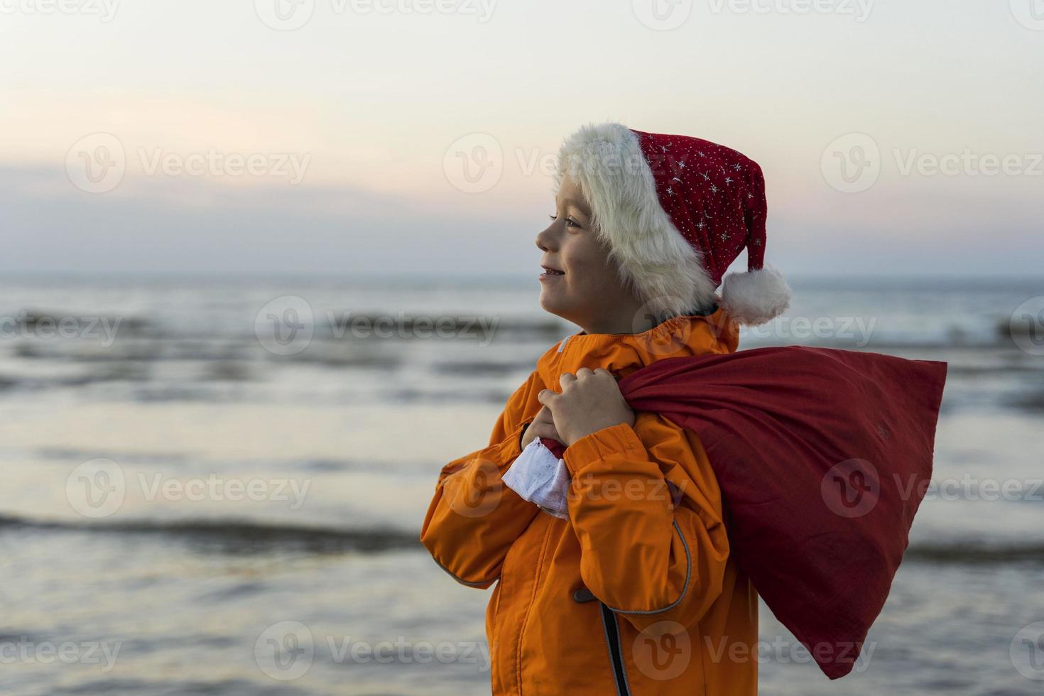 Porträt eines süßen Jungen in einer Kappe von st. Nikolaus, mit einer Tüte Weihnachts- und Neujahrsgeschenke foto