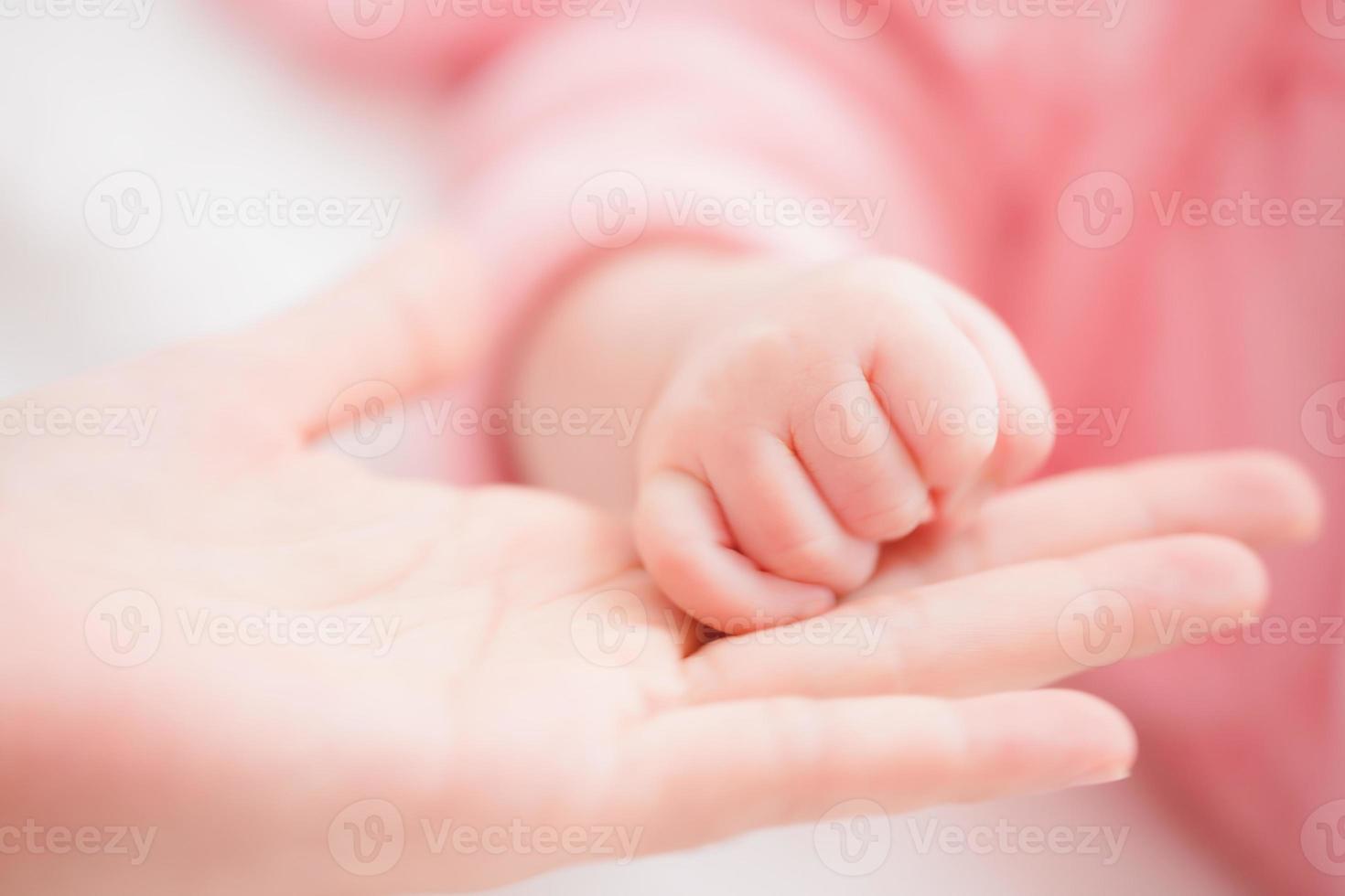Nahaufnahme Mutter Händchen haltend neugeborenes Mädchen in einem Raum. entzückendes kind ruht auf weißen bettlaken und starrt friedlich in die kamera. Säuglings-, Gesundheitswesen und Pädiatrie, Säuglingskonzept. foto