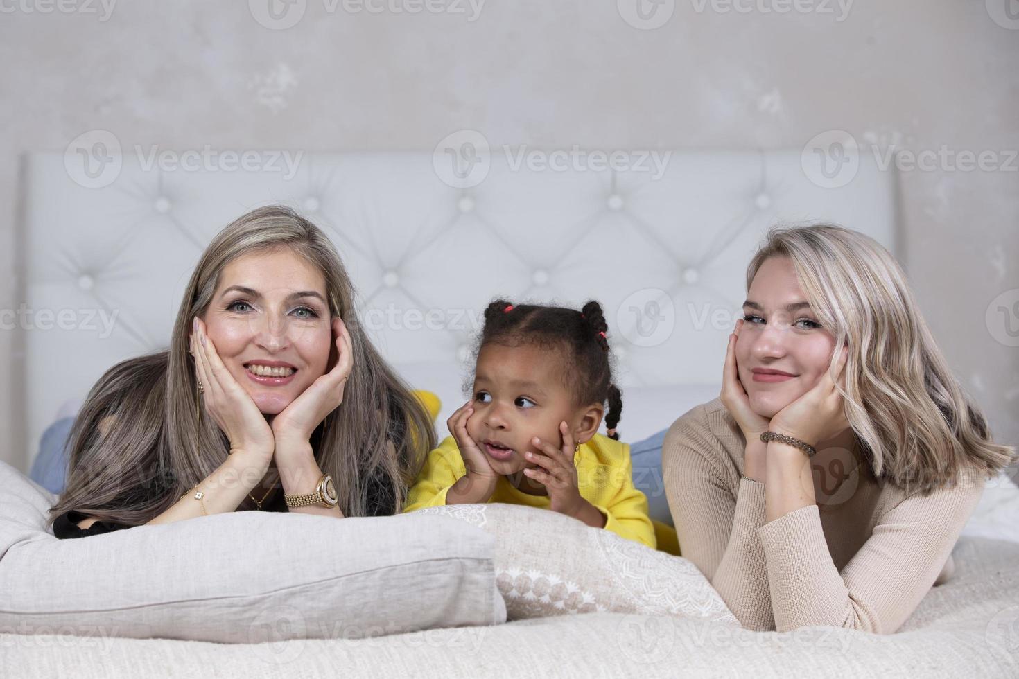 Familie aus verschiedenen Rassen. mutter großmutter hellhäutig und ein kleines afroamerikanisches mädchen liegen auf dem sofa. foto