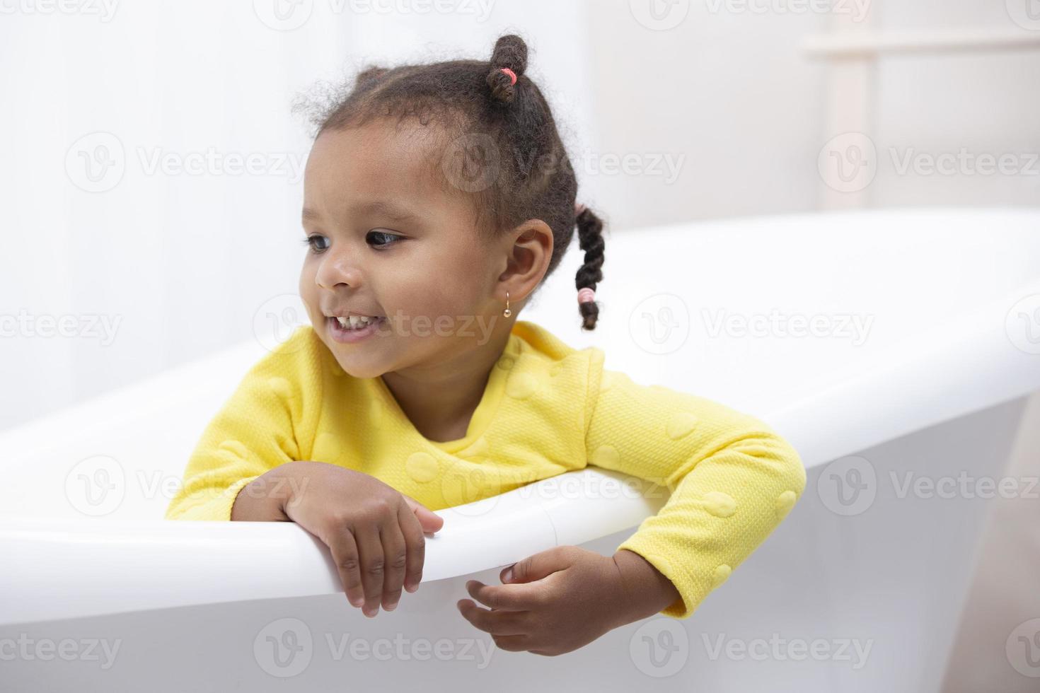 Kleines afroamerikanisches Mädchen in einem gelben Kleid mit lockigen Zöpfen sitzt in einem Retro-Bad. foto