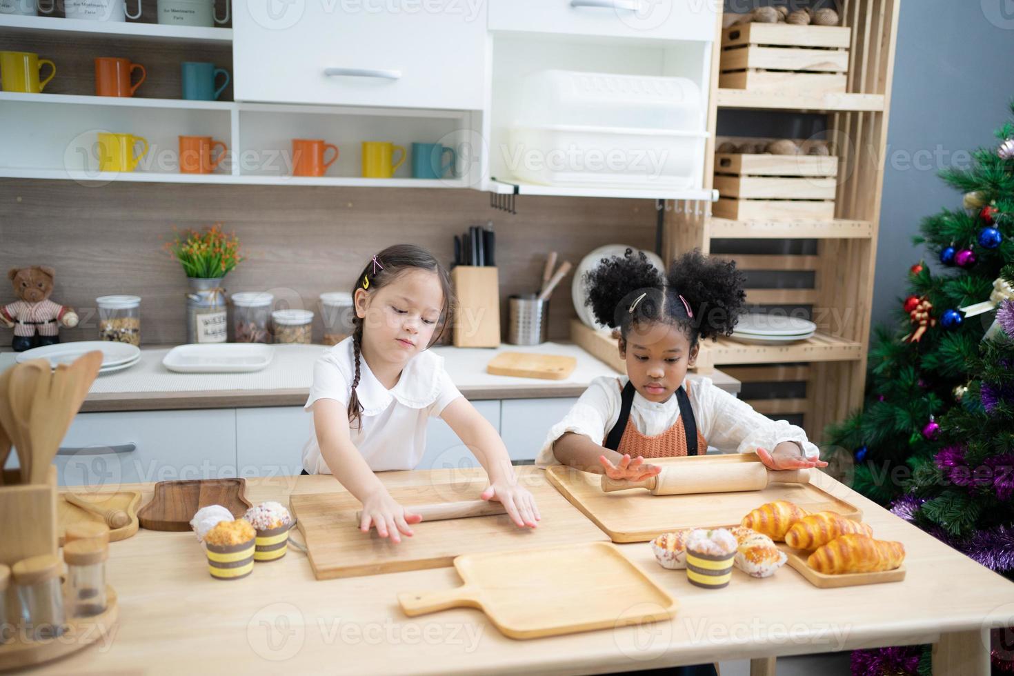 zwei glückliche kleine kinder, die zusammen kochen, teig ausrollen, an der holzarbeitsplatte in der modernen küche stehen, süß hausgemacht foto