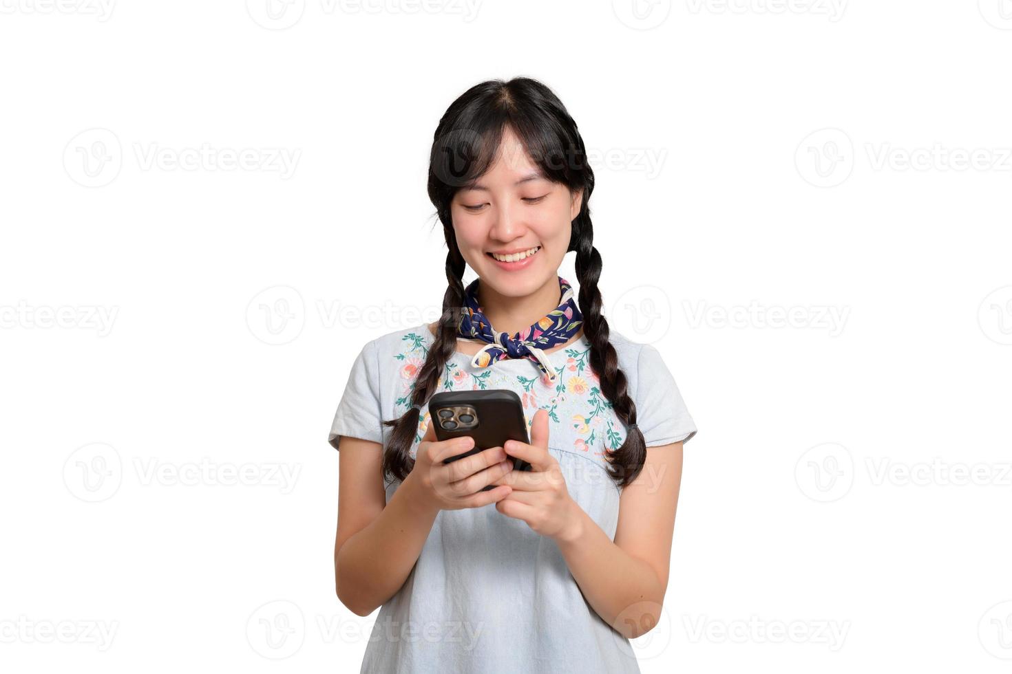 Porträt einer glücklichen, schönen jungen Asiatin im Jeanskleid mit einem Smartphone auf weißem Hintergrund. Studioaufnahme foto