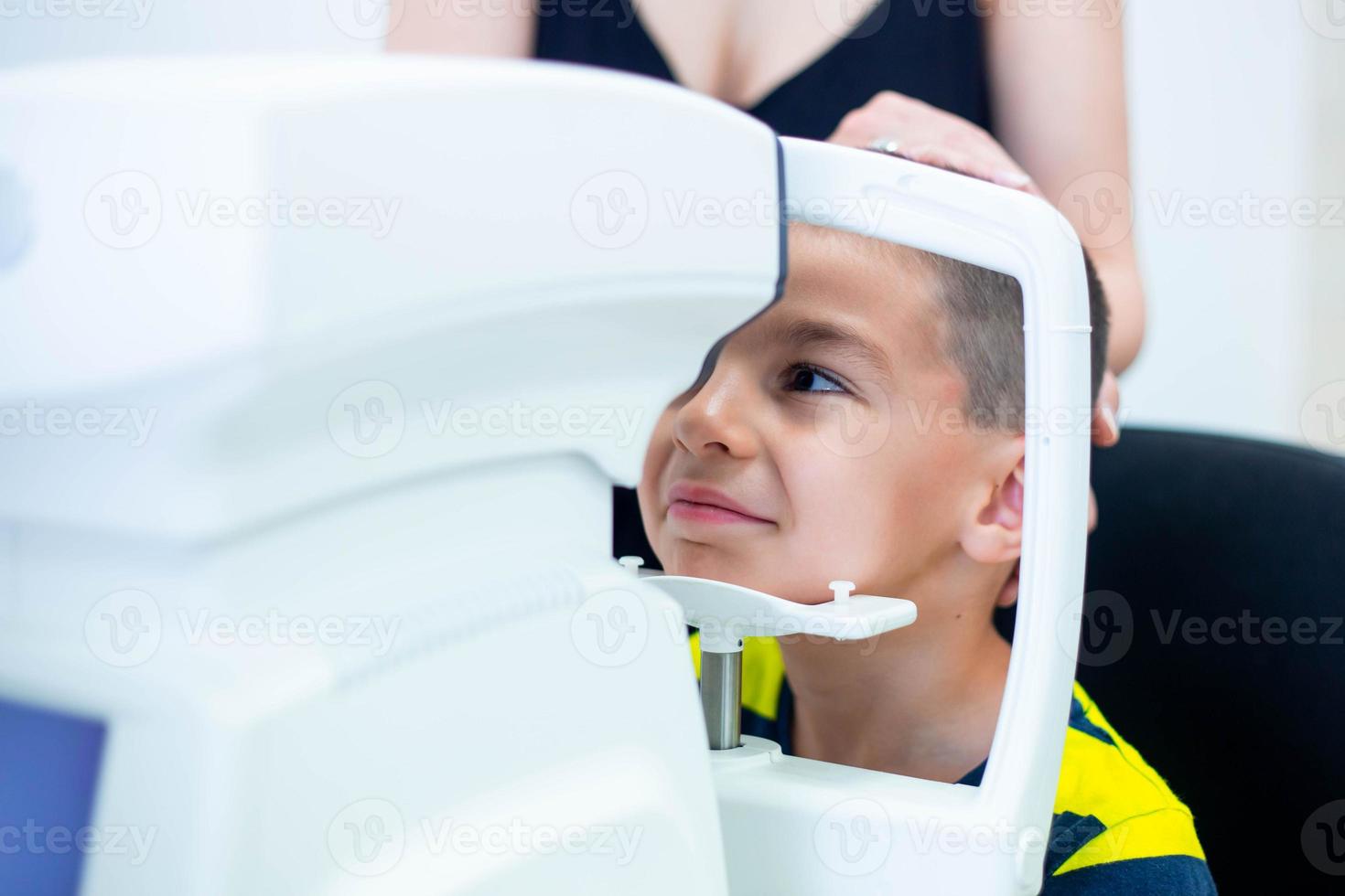 Augenärztin, die eine Maschine zur Überprüfung des Sehvermögens in der Klinik verwendet. kleiner Junge, der sich die Ausrüstung ansieht und die Augenpupille des Arztes im Optikgeschäft testet. konzept der augenpflege und gesundheit. foto