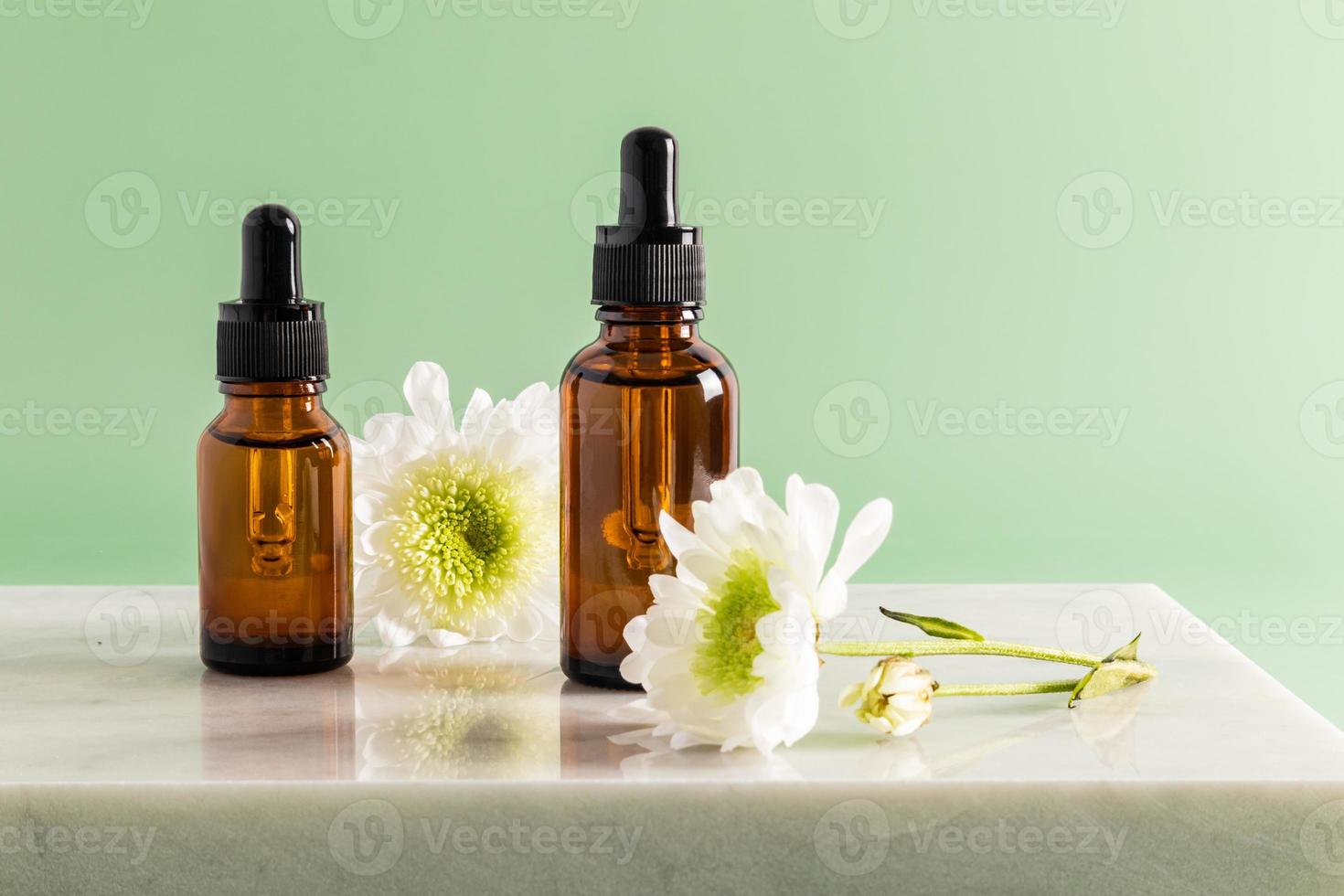 Auf einem Marmorpodium stehen zwei Kosmetikflaschen mit einem Tropfer mit einem Multivitamin-Feuchtigkeitsserum für das Gesicht. tägliche Pflege. grüner Hintergrund. foto