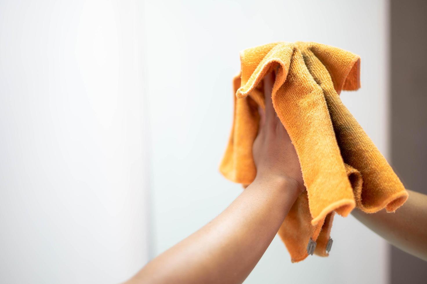 Weibliche Handreinigung und Abwischen des Spiegels mit orangefarbenem Mikrofasertuch im Wohnzimmer. Housekeeping-Konzept. foto