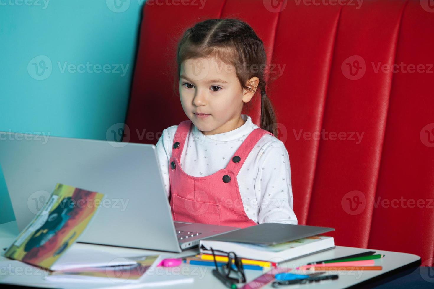 süßes kleines Mädchen mit Laptop zu Hause. zurück zum schulkonzept. das mädchen macht ihre hausaufgaben alleine auf dem laptop foto