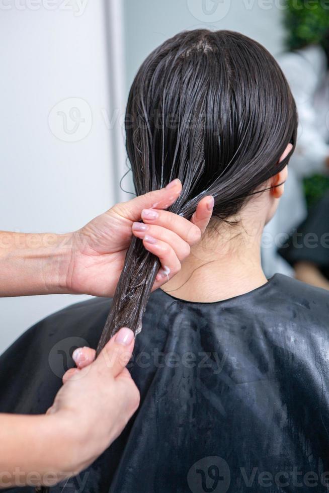 Friseur wendet eine Haarmaske auf glattes schwarzes Haar an. Haarpflege im Schönheitssalon. foto