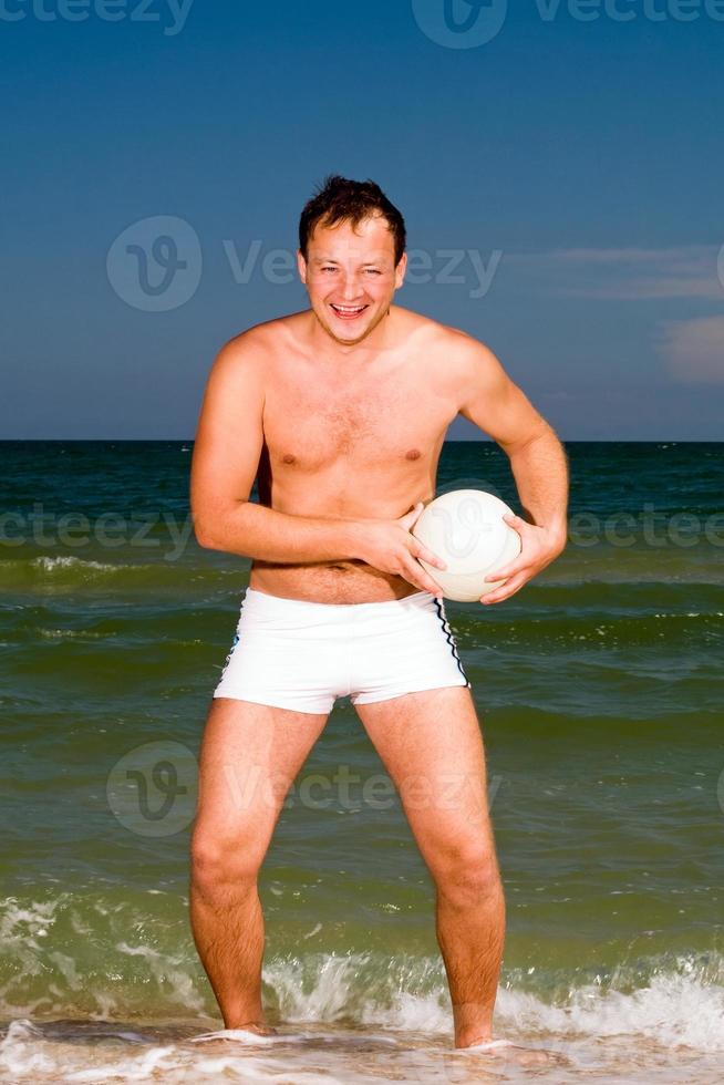 junger Mann, der einen Ball am Strand hält foto