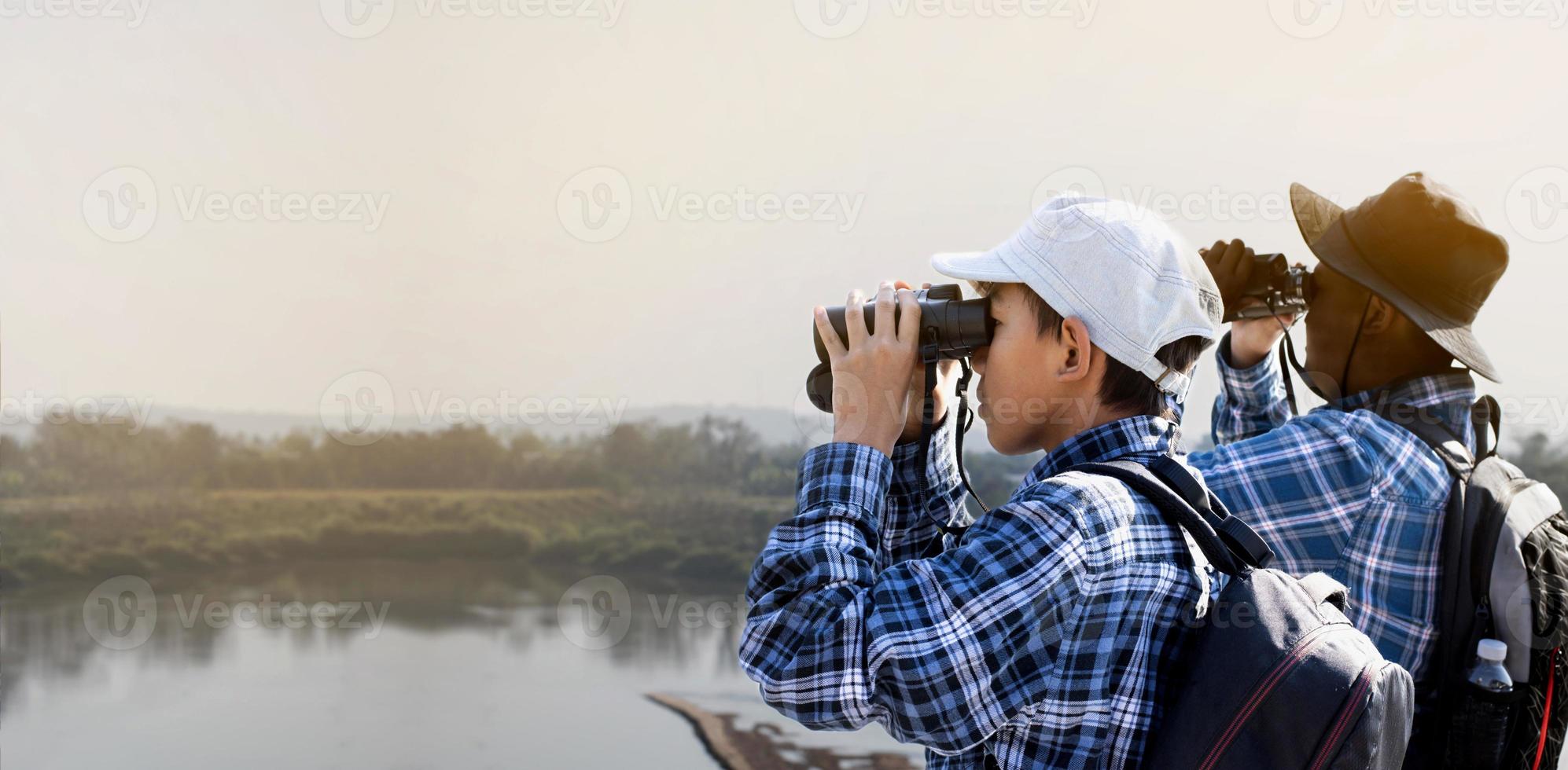 asiatische Jungen, die während des Sommercamps mit Ferngläsern Vögel auf Bäumen und Fische im Fluss im örtlichen Nationalpark beobachten, Idee zum Lernen von Kreaturen und Wildtieren und Insekten außerhalb des Klassenzimmers. foto