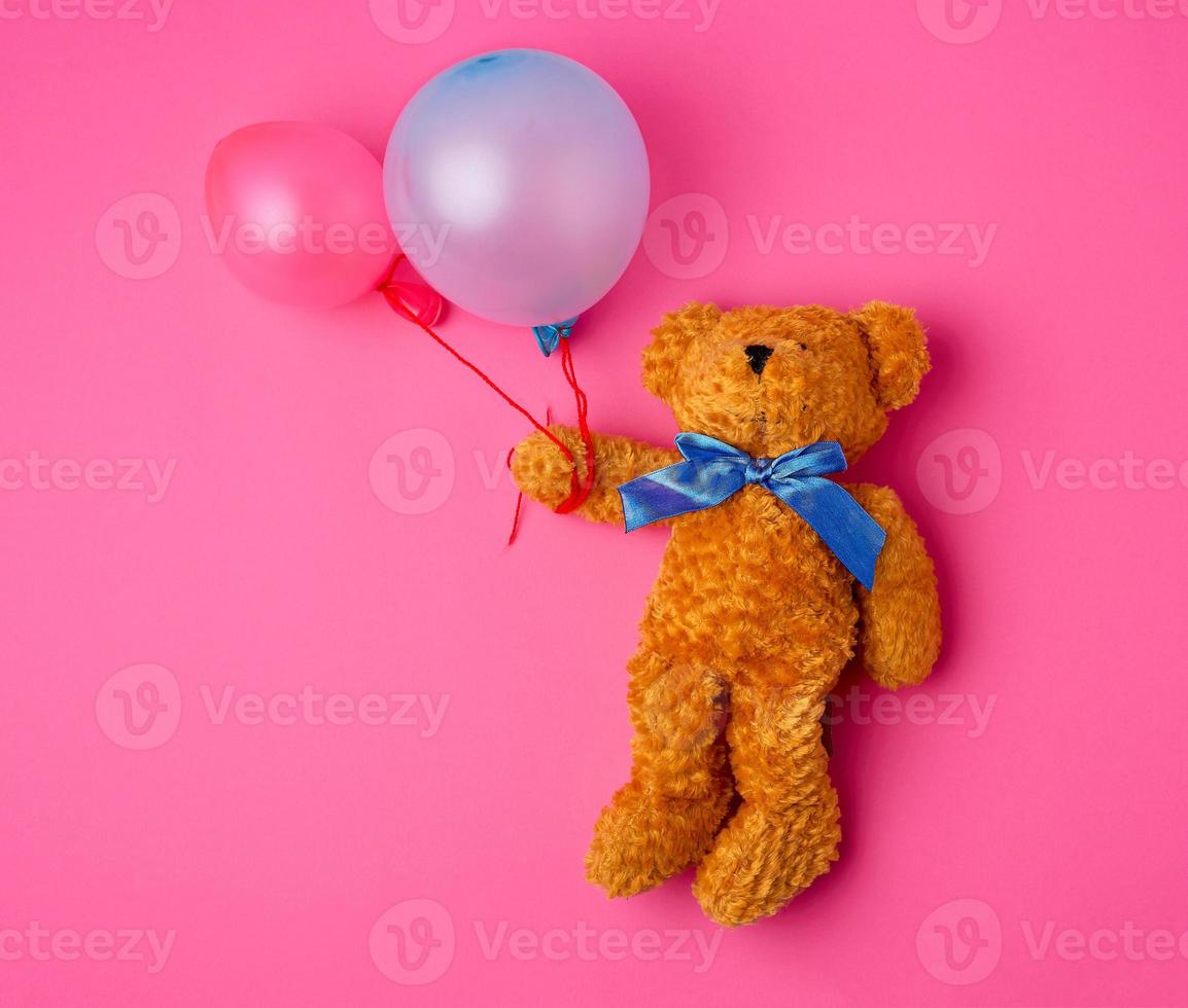 Der kleine braune Teddybär hält zwei aufgeblasene Luftballons an einem Seil foto
