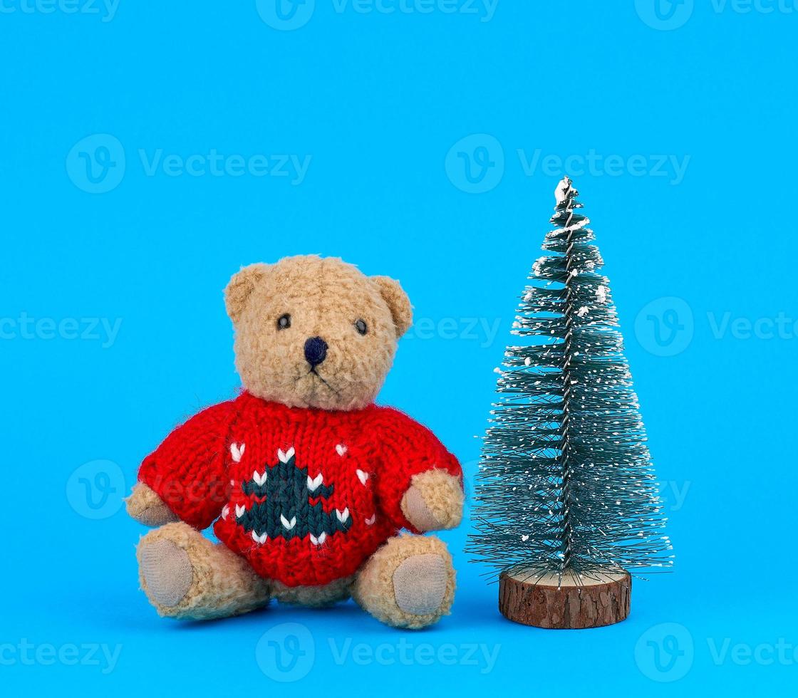 kleiner teddybär in einem roten weihnachtspullover und einem dekorativen baum foto