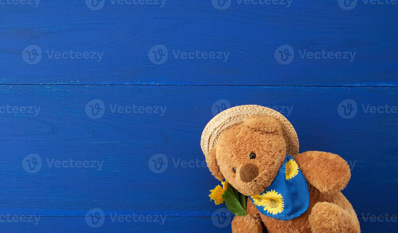 beiger Teddybär, der auf einem blauen Holzhintergrund sitzt foto