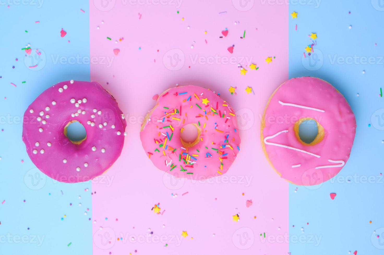 drei runde verschiedene süße donuts mit streuseln auf einem rosa-blauen hintergrund foto