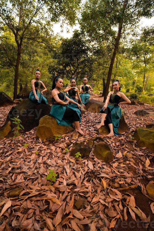 eine gruppe asiatischer frauen macht urlaub im wald, während sie einen grünen rock tragen und auf einem felsen sitzen foto