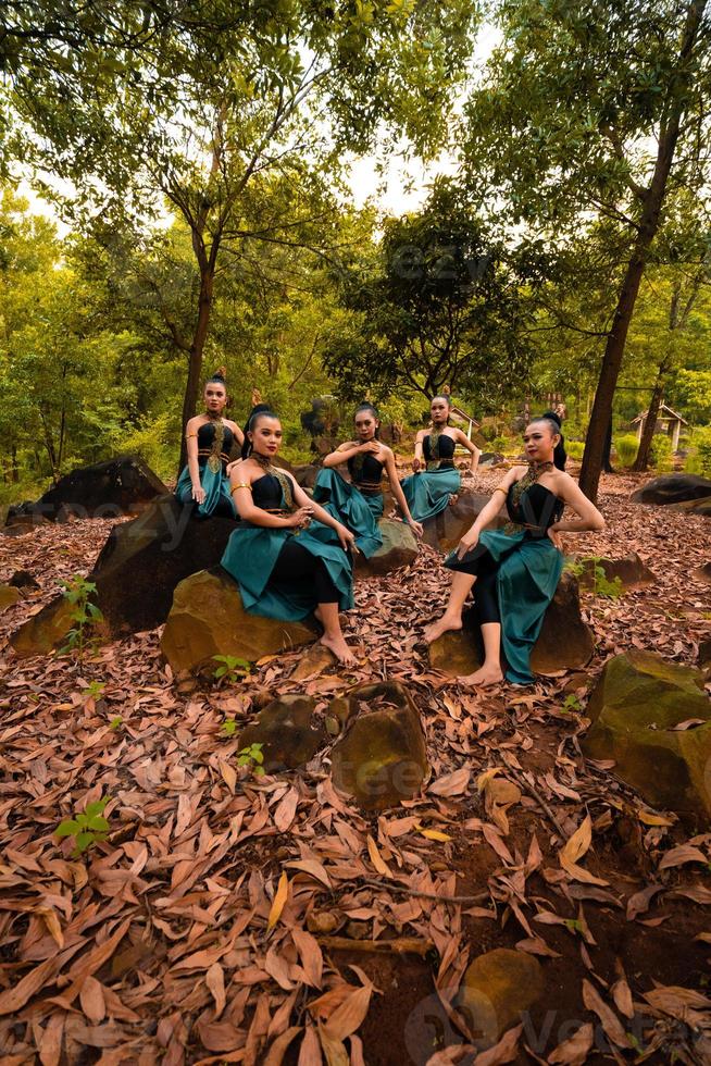 eine gruppe asiatischer frauen macht urlaub im wald, während sie einen grünen rock tragen und auf einem felsen sitzen foto