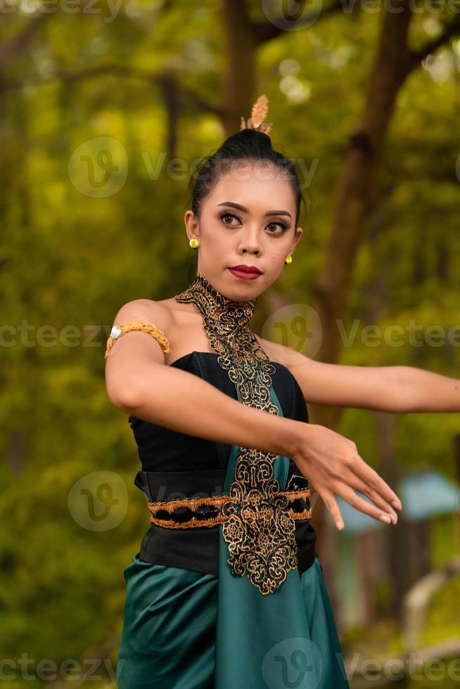 javanische Frau, die vor dem Wald in grünem Kostüm tanzt, während sie geschminkt ist und auftritt foto