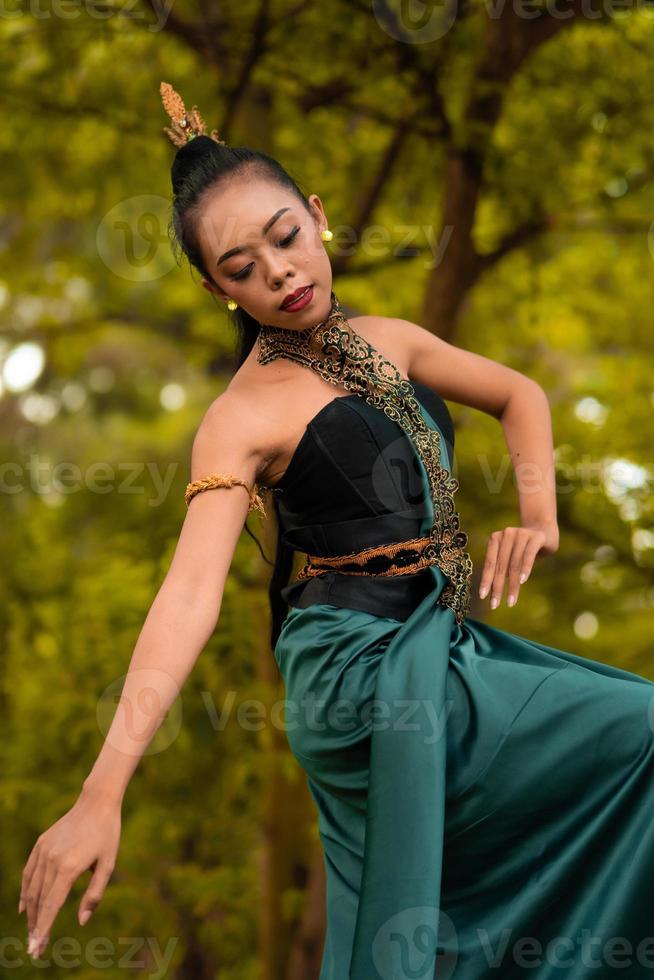 Porträt einer schönen asiatischen Frau in Make-up beim Tanzen vor dem Dschungel mit einem schwarz-grünen Kostüm auf ihrem Körper foto