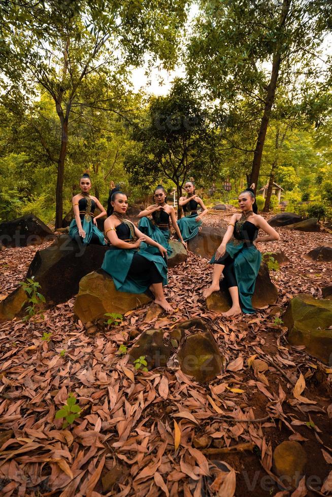 eine gruppe asiatischer frauen macht urlaub im wald, während sie einen grünen rock tragen und auf einem felsen sitzen foto