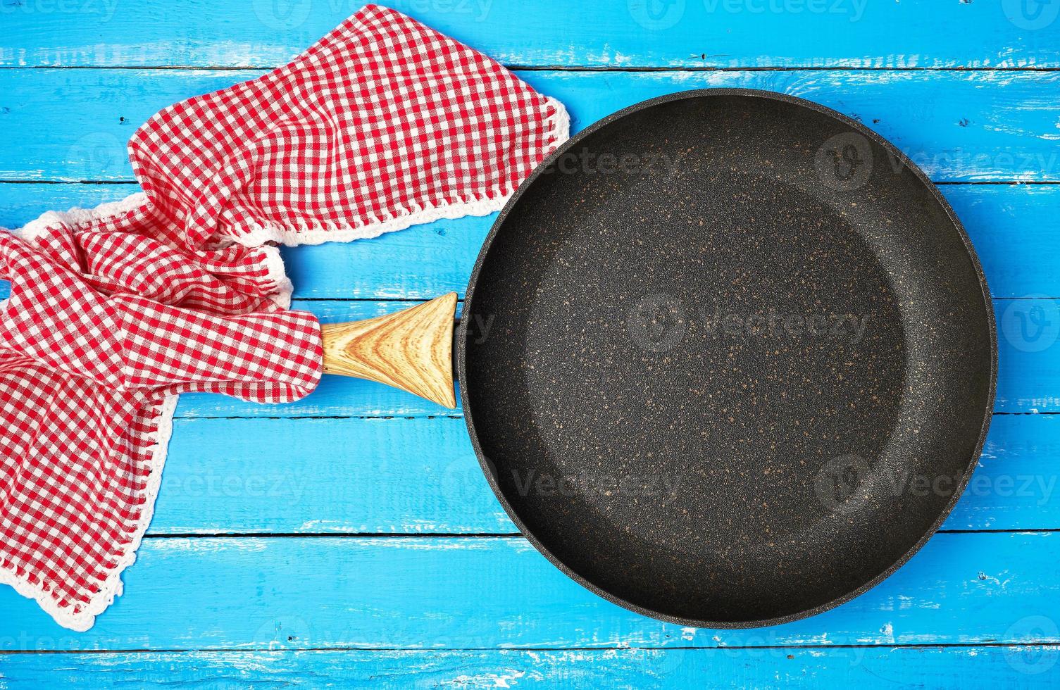 leere schwarze runde Bratpfanne mit Holzgriff und roter Küchenserviette foto