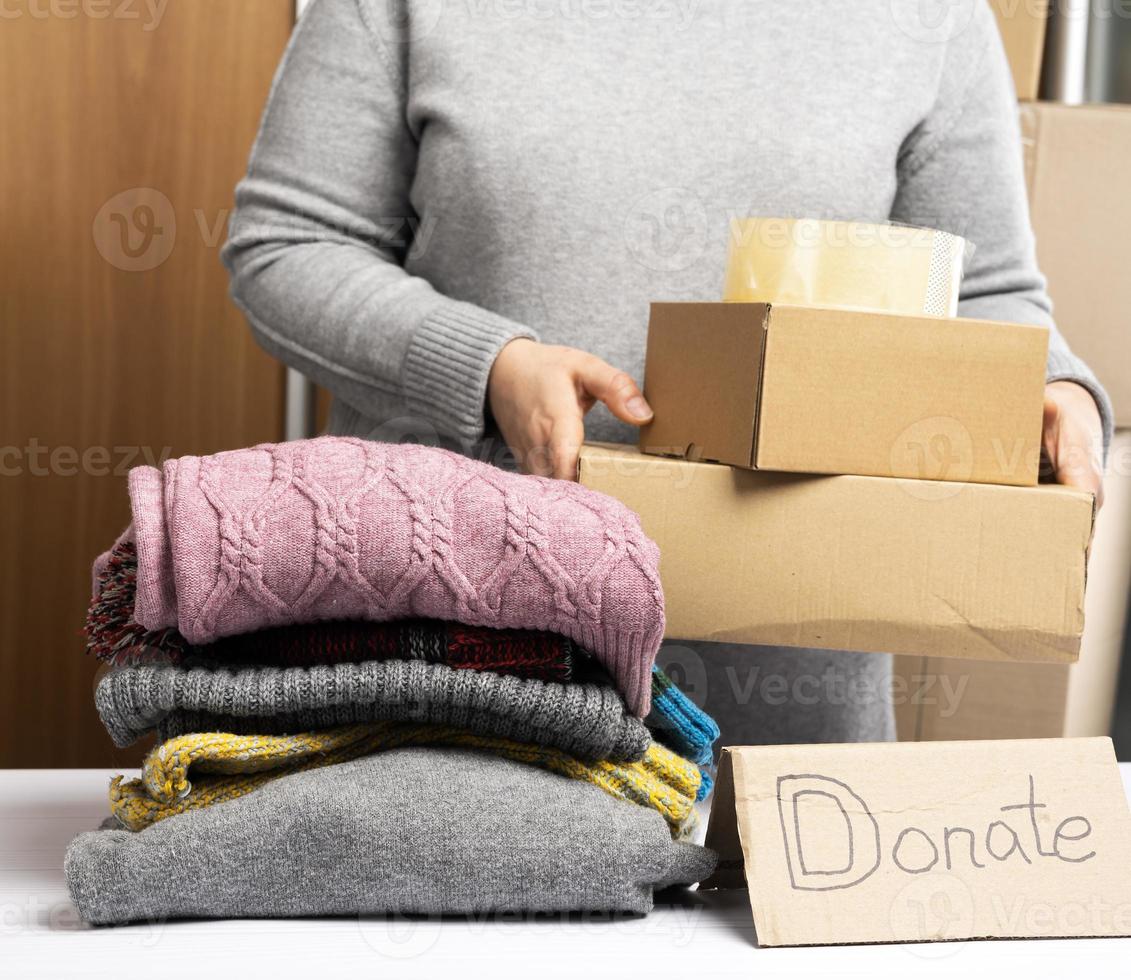 Frau in einem grauen Pullover packt Kleidung in eine Kiste, das Konzept der Unterstützung und Freiwilligenarbeit foto