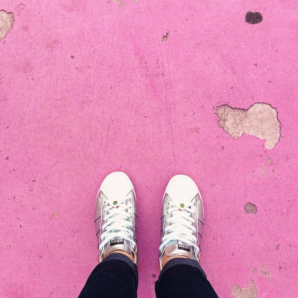 Person, die weiße Turnschuhe trägt, die auf rosa Boden stehen foto